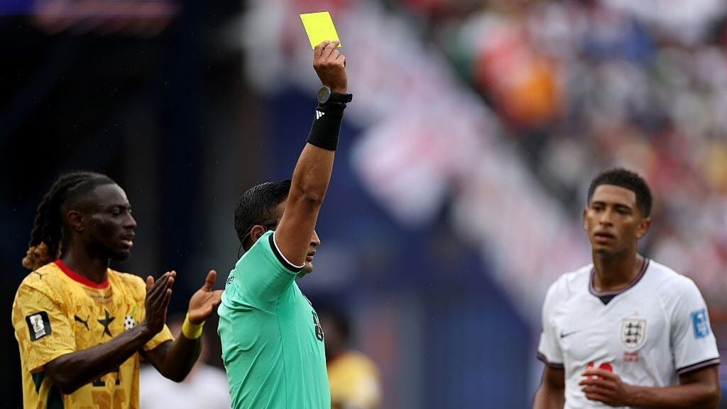 A referee holds a yellow card aloft during a 2026 World Cup match